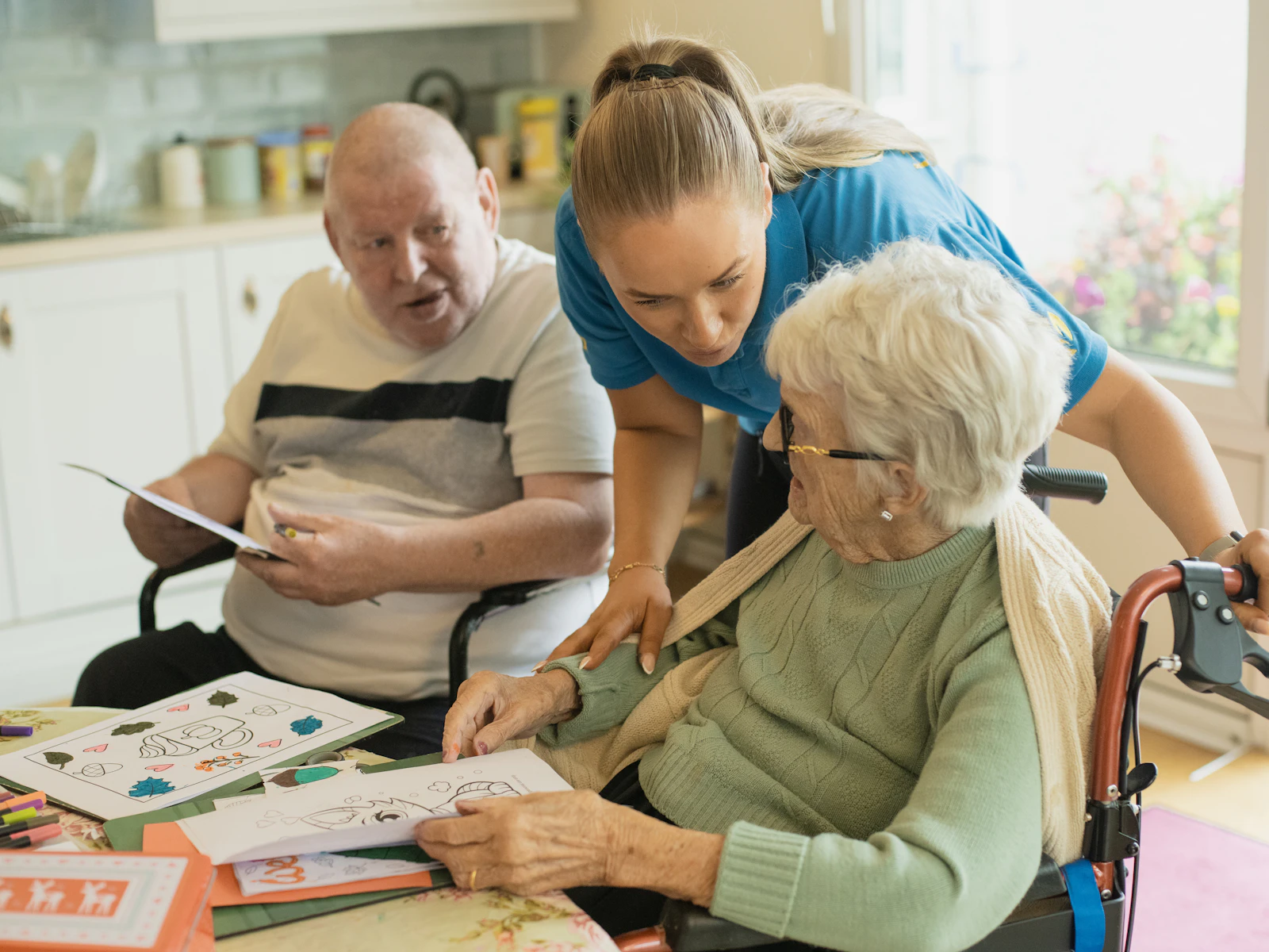 A caregiver sits with an elderly couple as they color together
