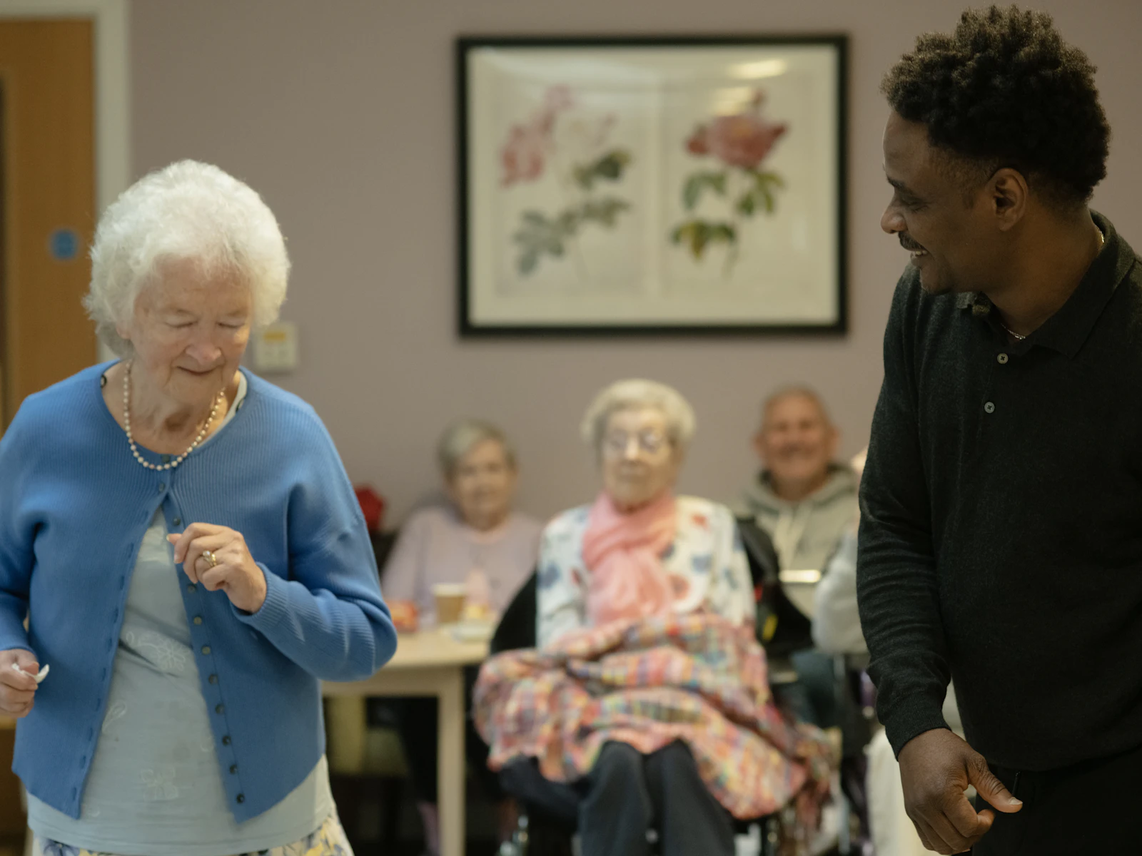A caregiver dances with a senior woman in a community room