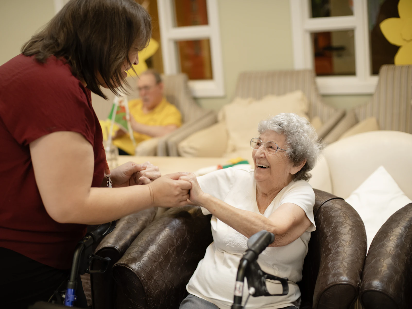 A caregiver holds hands with a smiling senior woman using a walker